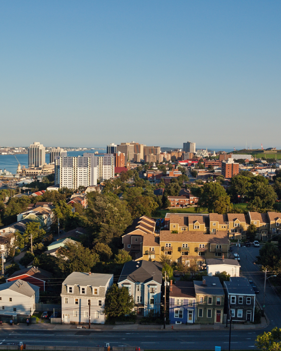 Cityscape with buildings and trees, featuring a body of water in the background.